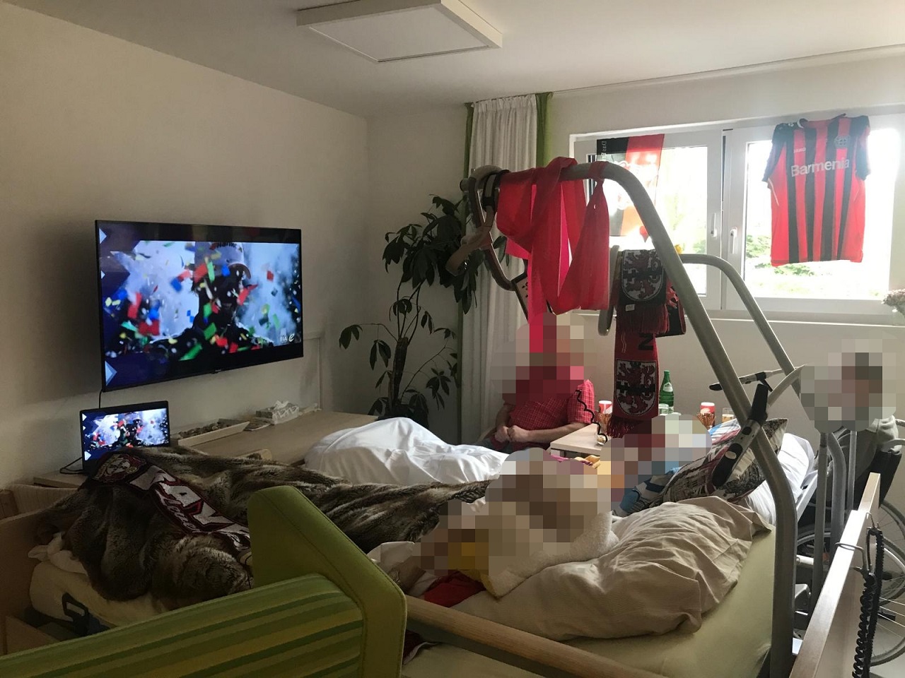Zwei Pflegebetten stehen vor einem großen Fernseher auf dessen Bildschirm gerade ein Konfettiregen heruntergeht,