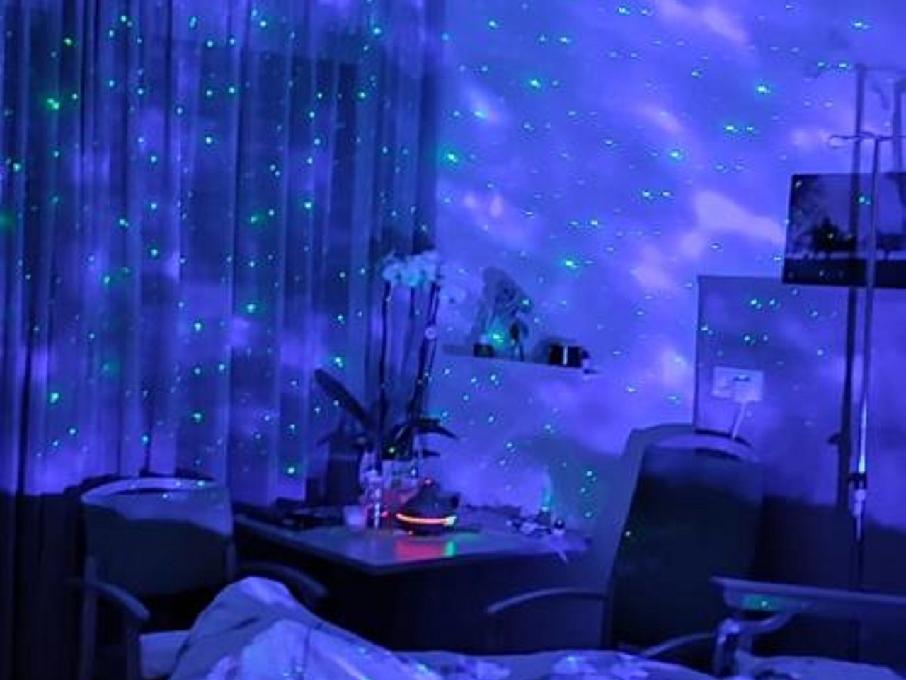 An eine Zimmerwand wird ein blauer Himmel mit grünen Sternenpunkten projiziert.
